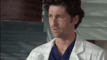 a man wearing a white lab coat and a blue scrub top looks at the camera .