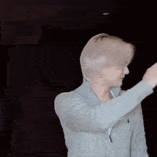 a man in a gray sweater is giving a thumbs up sign while standing in front of a black background .