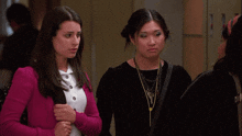 a woman in a pink cardigan stands next to another woman in a black shirt