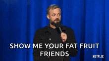 a man with a beard is holding a microphone on a stage and says show me your fat fruit friends .