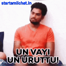 a man in an orange shirt is sitting on a couch with his arms crossed and says un vayi un urttu !