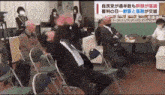 a group of people are sitting in folding chairs in a room and a man is sitting on the floor .