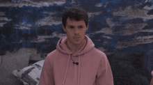 a man in a pink hoodie is standing in front of a blue wall and looking at the camera .