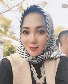 a woman wearing a scarf and a pearl necklace is smiling
