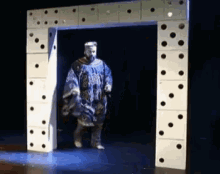 a man in a blue robe is walking through a domino archway on a stage .