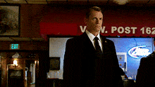 a man in a suit and tie stands in front of a red awning that says v. post 162