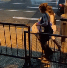 two women are walking down a sidewalk behind a fence at night