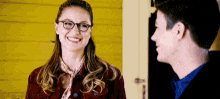 a man and a woman are standing next to each other and smiling . the woman is wearing glasses and a red jacket .