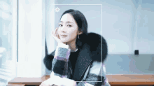 a woman in a plaid coat sits on a bench with her hand on her chin