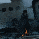 a woman sits on a box next to a fire with a first aid kit in the background