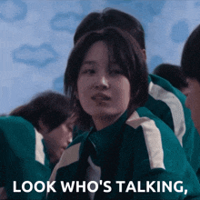 a girl in a green jacket with the words look who 's talking below her