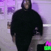 a man in a black hoodie is standing in a room with purple lights behind him .