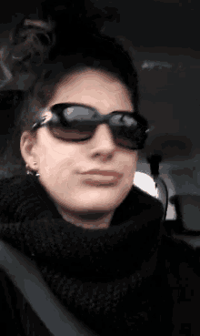 a woman wearing sunglasses and a black scarf is sitting in a car .