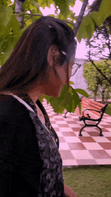a woman wearing glasses stands in front of a bench