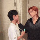 a man with red hair is holding a green object while another man holds a pen