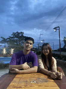 a man in a purple shirt sits next to a woman in a white shirt with the word believe on it