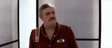 a man with a mustache is wearing a red jacket with a star trek patch on it