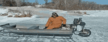 a man in an orange jacket is sitting in a boat with a motor attached to it .