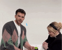 a man in a pink and green sweater is standing next to a woman in a black headband