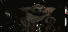 a baby yoda is sitting in a dark room and looking at the camera .