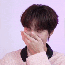 a young man wearing a pink sweater covers his mouth with his hand