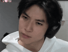 a man wearing headphones and a white hoodie looks at the camera