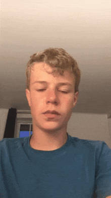 a young man wearing a blue shirt looks at the camera
