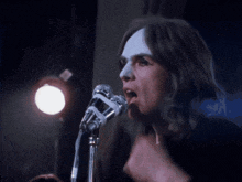 a woman singing into a microphone with a rubber band around her neck