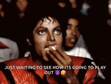 a man in a red jacket is eating popcorn while watching a movie in a theater .