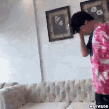 a man in a pink shirt is standing in front of a couch with mayward written on the bottom right