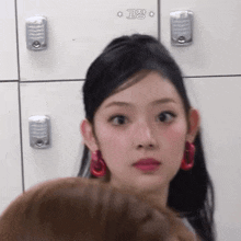 a woman wearing red earrings is looking at the camera in front of a locker .