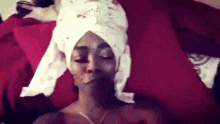 a woman with a towel wrapped around her head is laying in bed .
