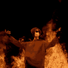 a man with his arms outstretched in front of a large fire