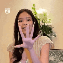 a woman wearing a white dress and purple nails is waving her hand