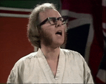 a man wearing glasses and a white shirt is standing in front of a british flag