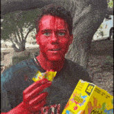 a man with red paint on his face is holding a box of gummy worms