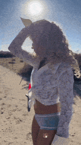 a woman in a white lace top and blue underwear is standing on a dirt road .