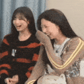 two young women are sitting next to each other laughing .