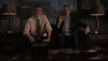 two men sit on a couch smoking cigars in a dark room