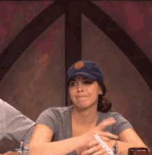 a woman wearing a baseball cap is sitting at a table holding a marker .