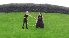 a man and a woman are playing with a hula hoop on a lush green field .