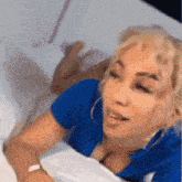 a woman in a blue shirt is laying in bed with her eyes closed