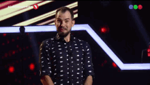 a man in a black and white shirt stands in front of a screen that says ' la voz argentina ' on it