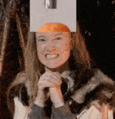 a woman wearing a fur coat is smiling with a picture of an orange on her head