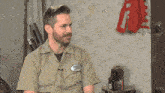 a man wearing a tan shirt with a patch on his chest that says ' simpson '