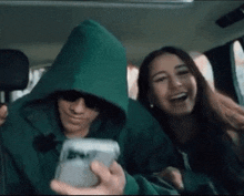 a man wearing a green hoodie is holding a cell phone next to a woman
