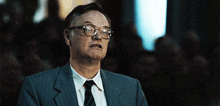 a man wearing glasses and a suit and tie looks at the camera