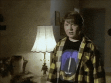 a boy in a plaid shirt stands in front of a lamp with a purple shirt on