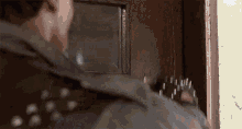 a man in a leather jacket is standing in front of a door with a gun in his hand .