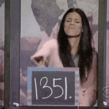 a woman is standing in front of a chalkboard with the number 1351 written on it .